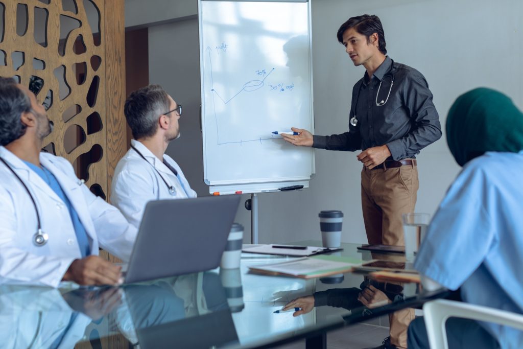 male doctor explaining graph on flip chart in meeting with medical team at hospital.